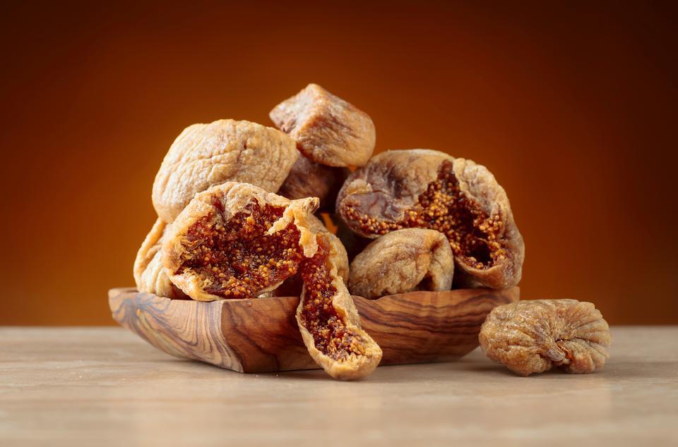 Dried figs in a old wooden dish on ceramic table.