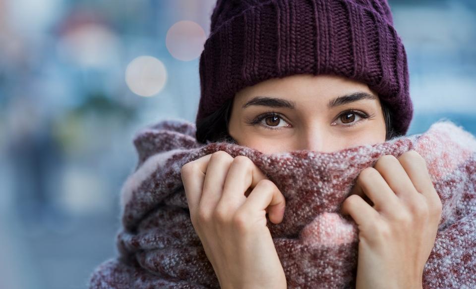 Winter portrait of young beautiful woman covering face with woolen scarf. Closeup of happy girl feeling cold outdoor in the city. Young woman holding scarf and looking at camera.
(Winter portrait of young beautiful woman covering face with woolen sca