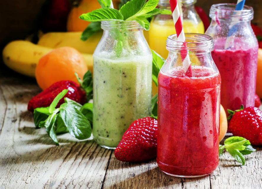 Multi-colored bottles with fresh fruit smoothies with striped straws, berries, fruit and mint leaves, vintage wooden background, selective focus